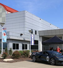 Modern automotive building with a sleek black sports car outside, vibrant atmosphere, clear skies, and fresh greenery.