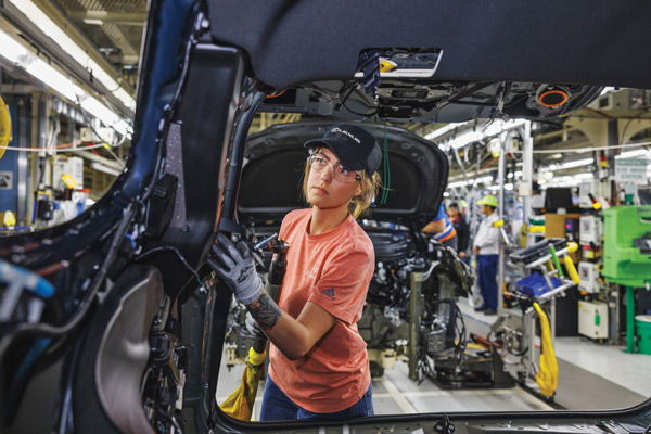 A worker in safety gear focuses on automotive manufacturing, surrounded by tools and machinery, reflecting determination and teamwork.