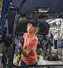 A worker in safety gear focuses on automotive manufacturing, surrounded by tools and machinery, reflecting determination and teamwork.