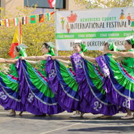 Festive dancers in vibrant green and purple attire showcase unity and joy at an international festival, celebrating culture.