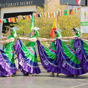 Festive dancers in vibrant green and purple attire showcase unity and joy at an international festival, celebrating culture.