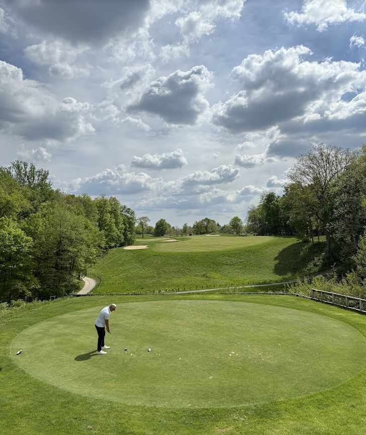 A golfer on the putting green, surrounded by lush greenery and hills, evokes calmness and tranquility in a bright setting.