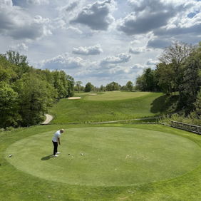 A golfer on the putting green, surrounded by lush greenery and hills, evokes calmness and tranquility in a bright setting.