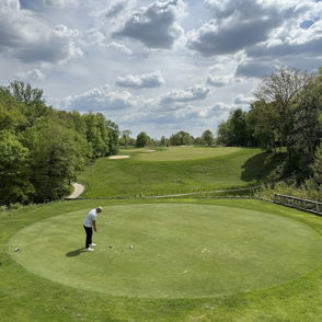 A golfer on the putting green, surrounded by lush greenery and hills, evokes calmness and tranquility in a bright setting.