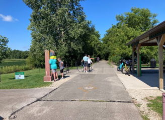 Scenic park pathway with people, bicycles, lush greenery, and a sunny sky, evoking tranquility, joy, and community connection.
