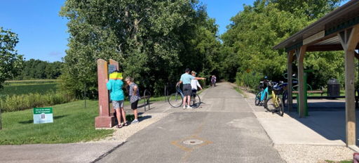 Scenic park pathway with people, bicycles, lush greenery, and a sunny sky, evoking tranquility, joy, and community connection.