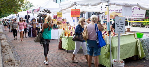 A lively outdoor market with white tents, colorful signs, and people browsing, evoking community joy and excitement.