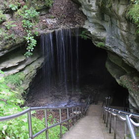 A serene cave entrance with lush greenery and a waterfall, inviting exploration and evoking tranquility and wonder.