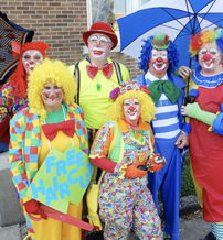 Colorful clowns in playful costumes pose joyfully at an outdoor event, evoking fun and community vibes.