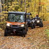Two ATVs navigate a winding trail through vibrant autumn scenery with colorful leaves, evoking adventure and camaraderie.