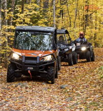 Two ATVs navigate a winding trail through vibrant autumn scenery with colorful leaves, evoking adventure and camaraderie.