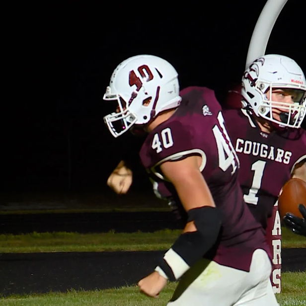 Three football players in maroon and white uniforms celebrate a successful play under the dark sky, exuding joy and camaraderie.