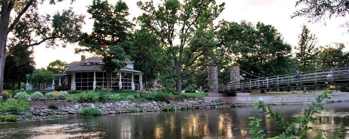 Serene outdoor scene with tranquil water, lush greenery, a cozy building, and a wooden bridge, evoking peace and relaxation.