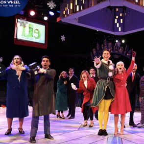 Festive theater scene with colorful costumes and joyful ensemble captures holiday spirit and community celebration.