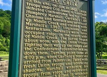 Historical marker for the Battle of Middle Creek, 1862, set against a serene backdrop of blue sky and green trees.