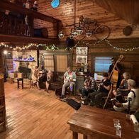Cozy cabin setting with warm lighting, live music, engaged guests, evoking joy, connection, and a celebratory atmosphere.