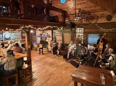 Cozy cabin setting with warm lighting, live music, engaged guests, evoking joy, connection, and a celebratory atmosphere.
