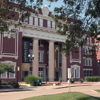 Brick building with tall columns, likely a museum or library, surrounded by greenery, bright lighting, and an inviting atmosphere.