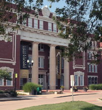 Brick building with tall columns, likely a museum or library, surrounded by greenery, bright lighting, and an inviting atmosphere.