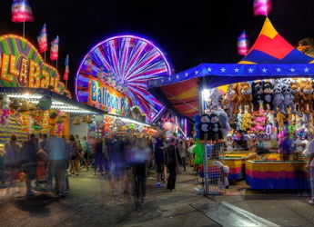 A vibrant night carnival scene with glowing lights, bustling crowds, game booths, food stalls, and a Ferris wheel.
