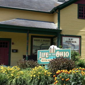 Charming yellow house with green accents, colorful garden, and lush lawn creates a warm, inviting atmosphere.