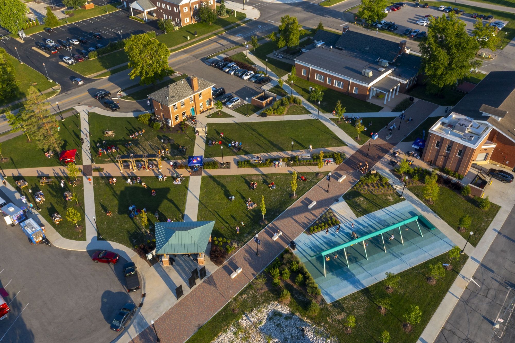 Aerial view of a vibrant community area with green spaces, pathways, and people, reflecting joy, serenity, and activity.