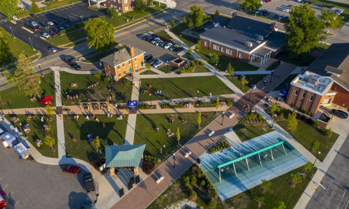 Aerial view of a vibrant community area with green spaces, pathways, and people, reflecting joy, serenity, and activity.