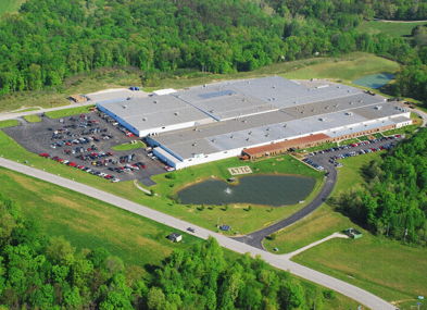 Aerial view of an industrial building with greenery, a parking lot, and a tranquil pond, evoking efficiency and serenity.