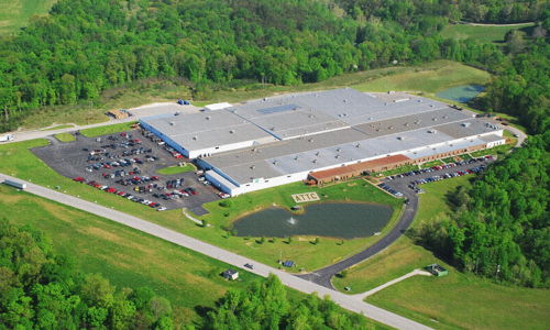 Aerial view of an industrial building with greenery, a parking lot, and a tranquil pond, evoking efficiency and serenity.