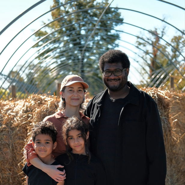 A joyful family of four poses together outdoors by hay bales, showcasing happiness and connection in a natural setting.