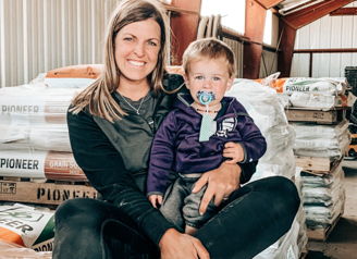 A woman and child sit in a rustic storage space, radiating warmth and happiness in a nurturing, familial moment.