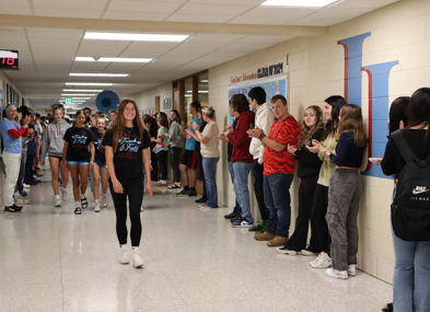 Students cheer in a school hallway as one confidently walks through, embodying excitement and community spirit.