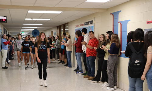Students cheer in a school hallway as one confidently walks through, embodying excitement and community spirit.