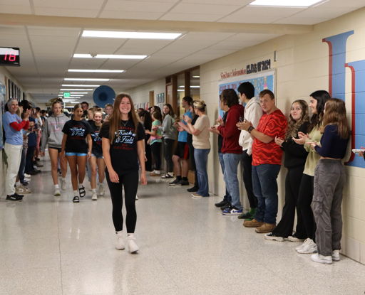Students cheer in a school hallway as one confidently walks through, embodying excitement and community spirit.