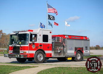 A red fire truck parked under a blue sky, displaying flags, symbolizes safety, community, and patriotism on a bright day.