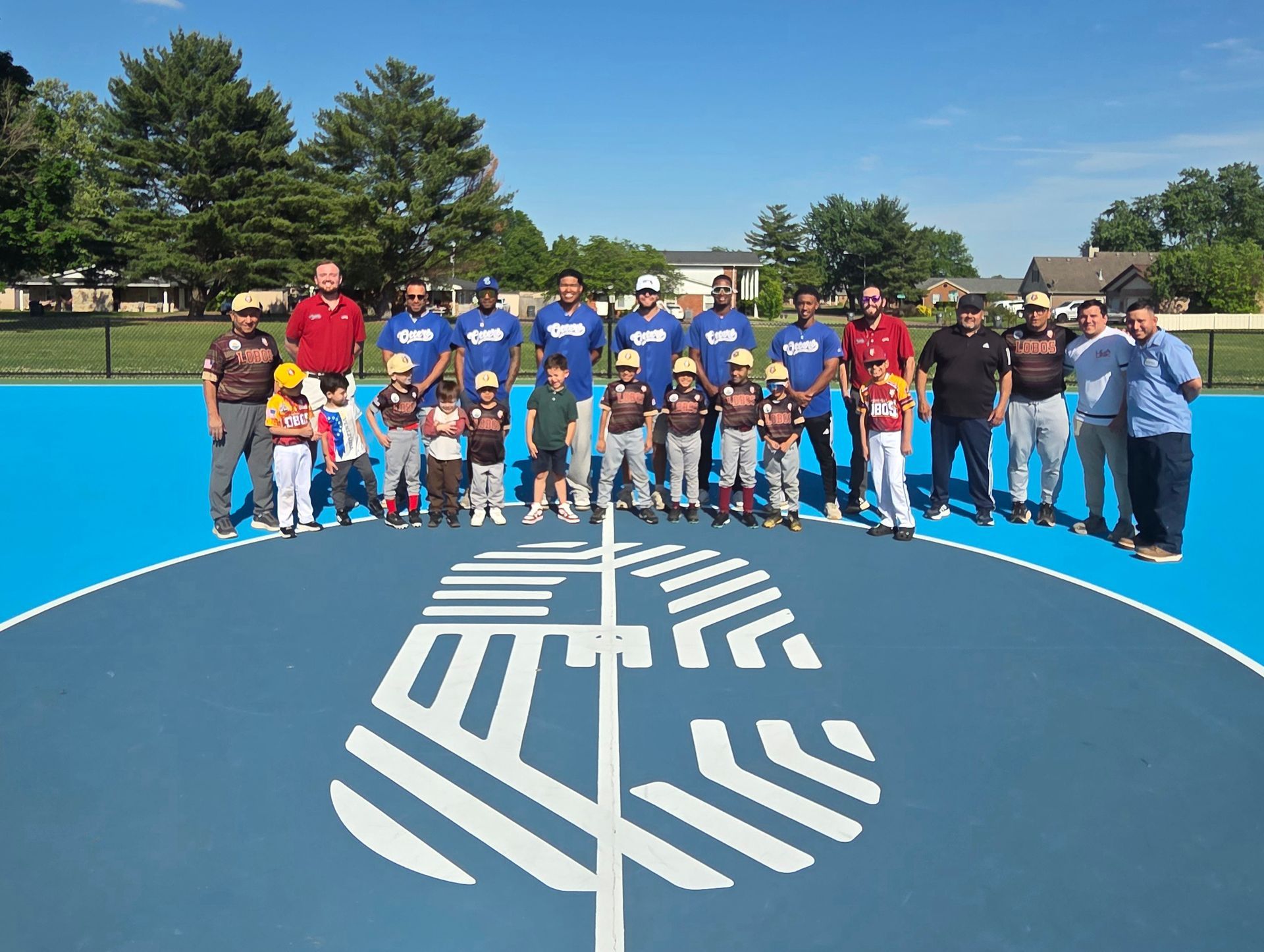 A joyful community gathering on a bright blue basketball court, featuring smiling adults and children enjoying the day.