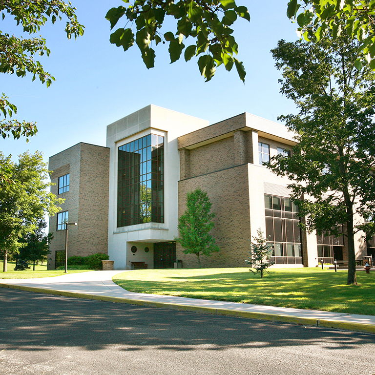 Modern educational building amidst greenery, featuring clean lines, large windows, and a tranquil, inviting atmosphere.