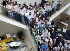 A vibrant office gathering shows unity and professionalism, with many wearing masks, highlighting health awareness and positivity.