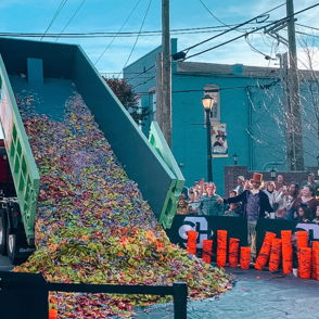 A truck unloads colorful candy at a lively outdoor event, evoking joy and excitement among gathered spectators.
