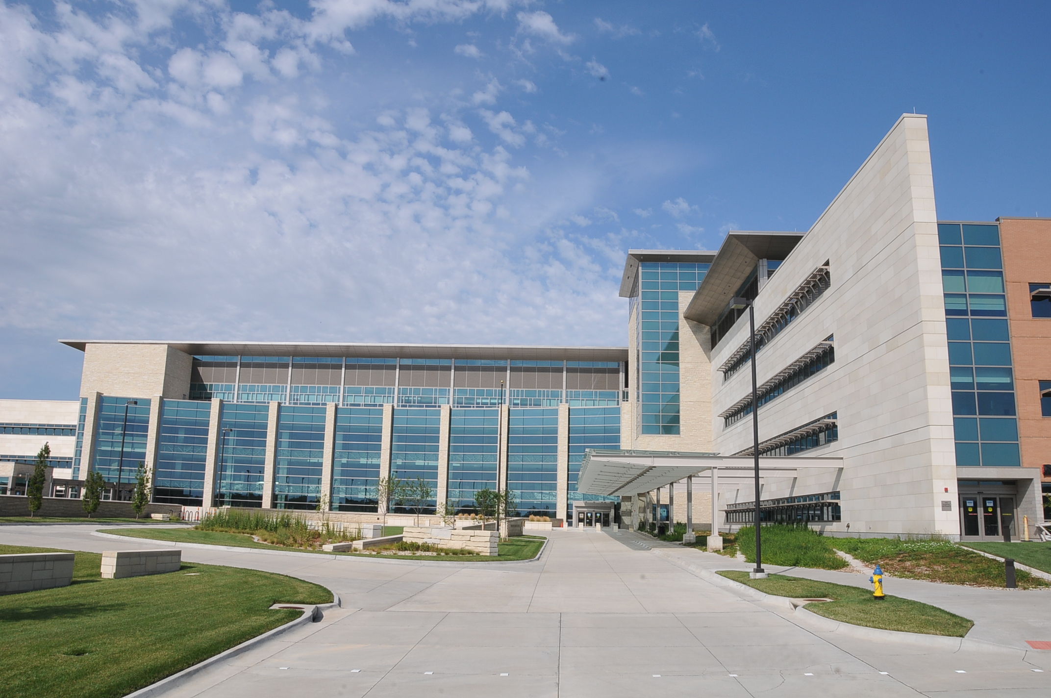 Modern multi-story building with glass and concrete, large windows, manicured lawns, and a bright sky, suggesting professionalism.