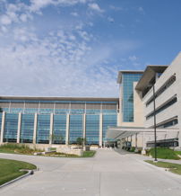 Modern multi-story building with glass and concrete, large windows, manicured lawns, and a bright sky, suggesting professionalism.