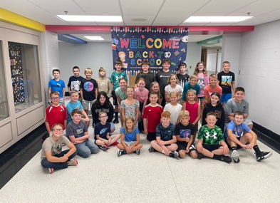 Students gather in a school hallway under a "WELCOME BACK TO SCHOOL" banner, expressing excitement and community spirit.