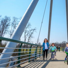 A family of four smiles on a bridge, enjoying a sunny day surrounded by greenery, conveying joy and togetherness.