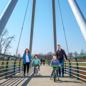 A family of four smiles on a bridge, enjoying a sunny day surrounded by greenery, conveying joy and togetherness.