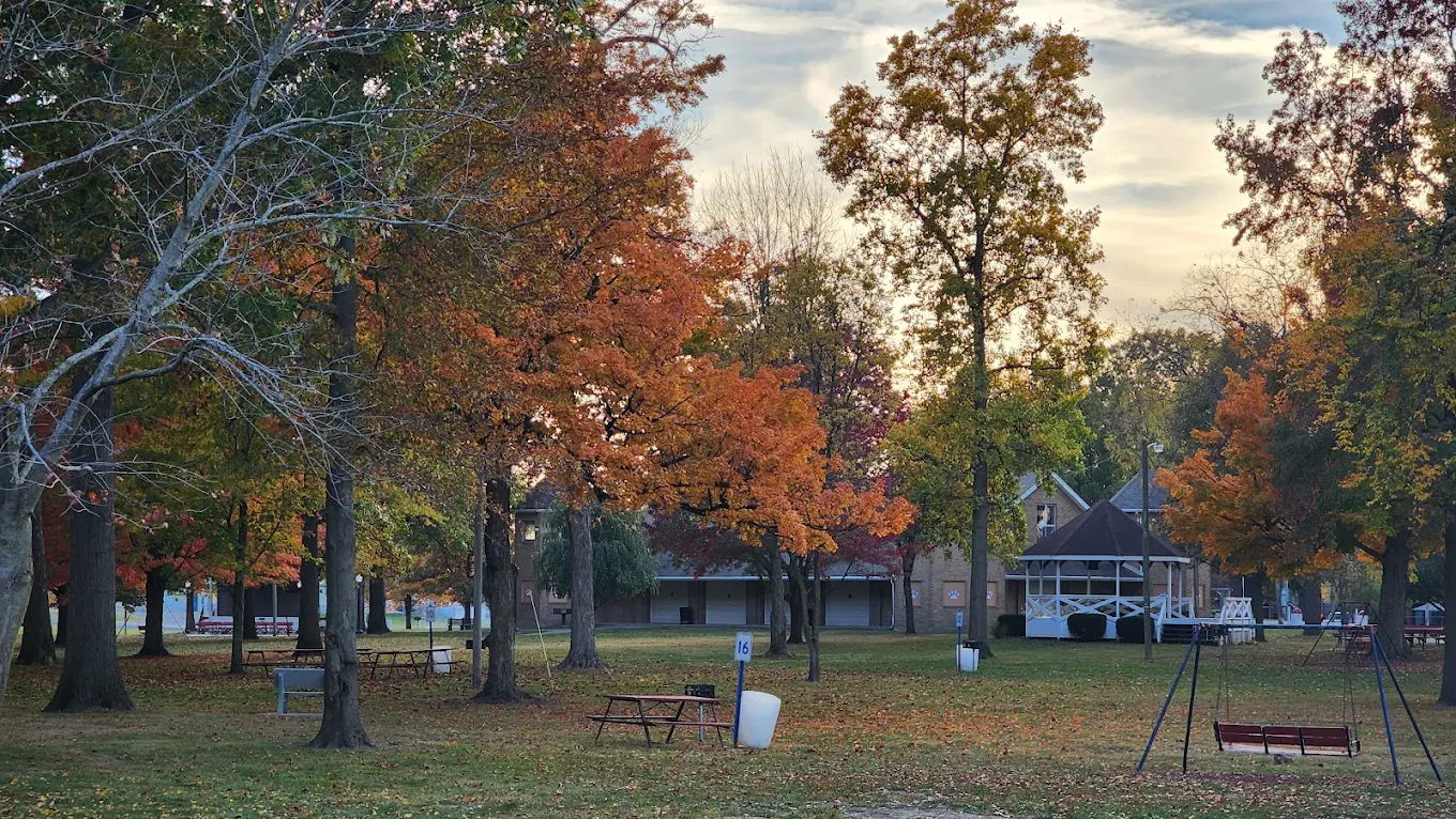 Serene park scene with vibrant autumn trees, grass, benches, swings, and a gazebo, evoking tranquility and nostalgia.