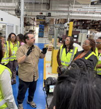 Group in safety vests engaged in a presentation in a warehouse, highlighting teamwork and a positive learning environment.