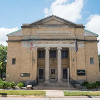 Classical brick building with columns, flags, and greenery, evoking community pride and nostalgia on a sunny day.