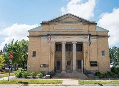 Classical brick building with columns, flags, and greenery, evoking community pride and nostalgia on a sunny day.