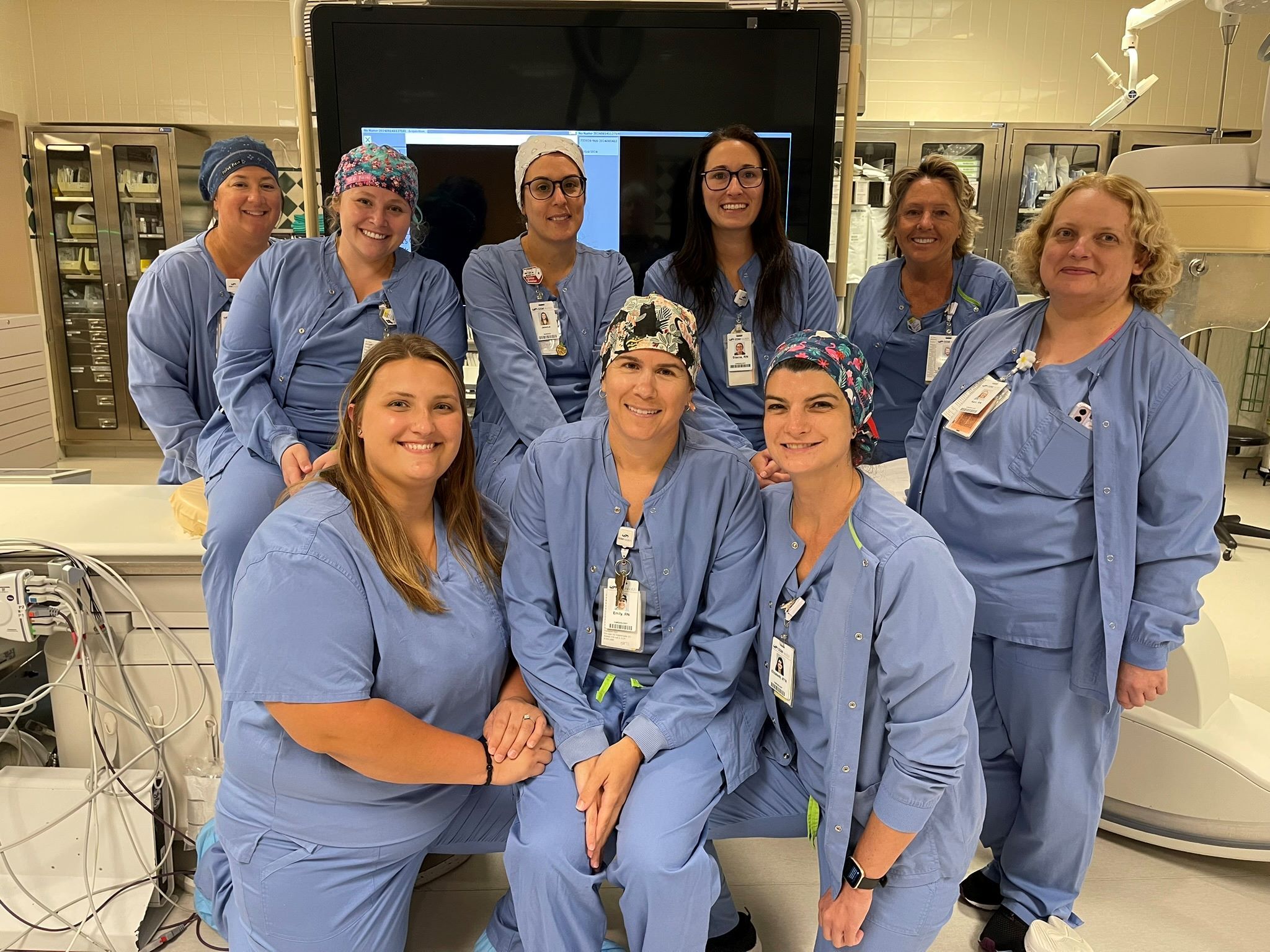 Ten women in blue scrubs smile in a semi-circle, showcasing teamwork and camaraderie in a medical setting.