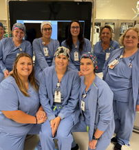 Ten healthcare professionals in blue scrubs and caps smile together, showcasing teamwork and a supportive clinical atmosphere.